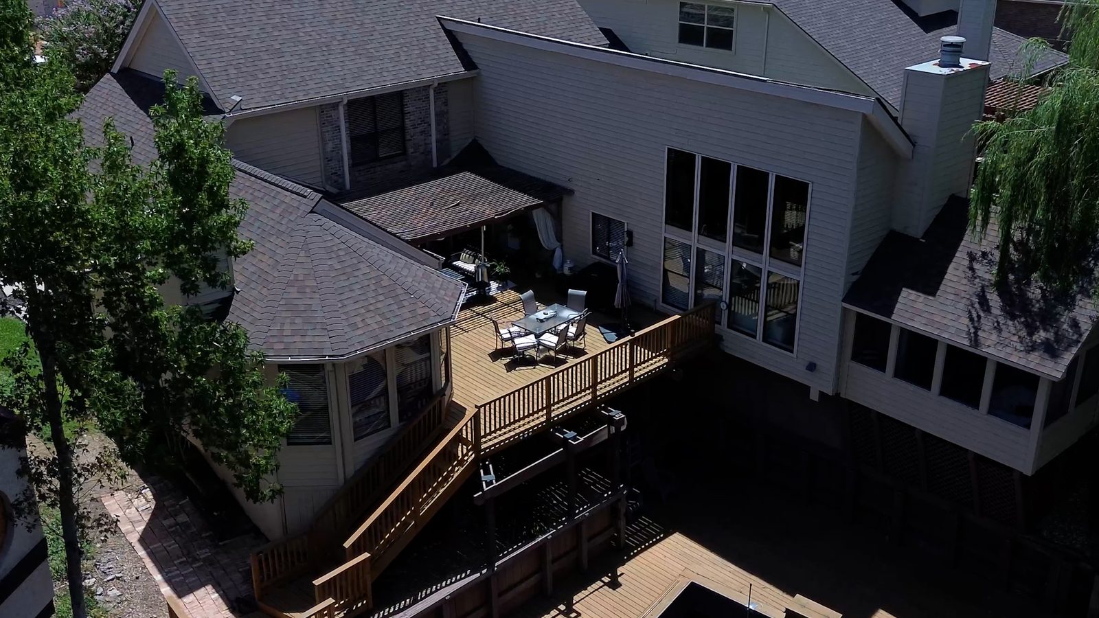 Aerial view of the back of the home, with a raised wooden deck and patio table below a wall of tall windows